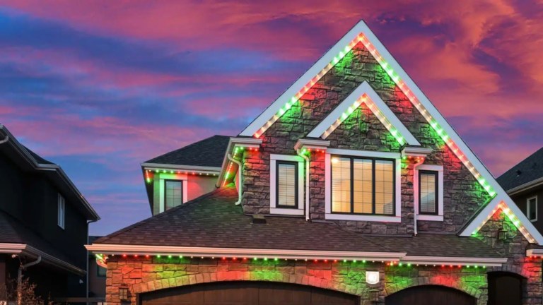 A 2 story house is lit up in red and green for Christmas with Gemstone permanent LED pot lights.