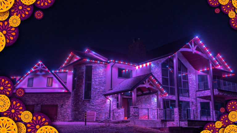 A multi-story house is lit up with multi-coloured lights. There is a festive orange and pink floral border around the corners of the image.