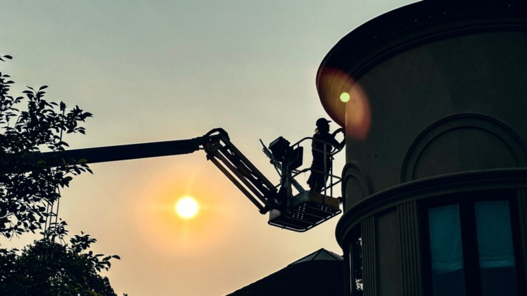 A Vibe Illuminations worker stands on an elevated lift as they install Gemstone Lights Outdoor LED Lights to the soffits of a tall Residential Building.