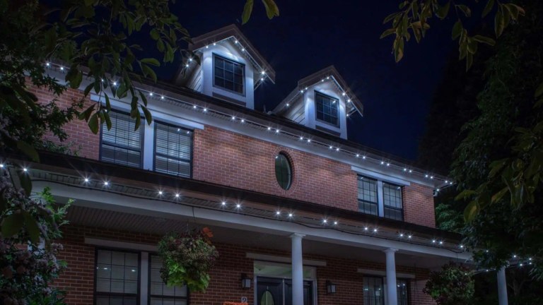 Two story red brick home with illuminated white LED lights around 2 dormers and and two roof levels.