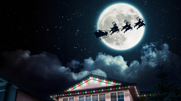 Santa rides his sleigh with reindeer in front of a full moon on a dark starry night. A white 2 storey home below is lit up with red and white Gemstone lights. The words On the blog, why Santa prefers to visit houses with Gemstone lights is written on the bottom.