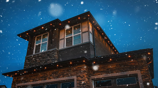 A 2 storey house illuminated with Gemstone Lights with snow falling in the picture.