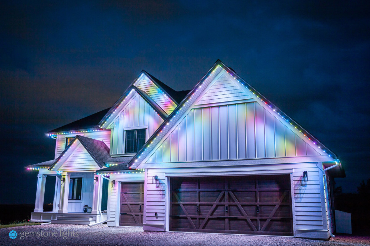 A white house illuminated in alternating pink, green, yellow, and blue Gemstone Lights programmable outdoor lights.